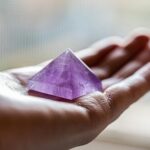 Close-up of an amethyst pyramid crystal resting in an open hand, captured in soft lighting.